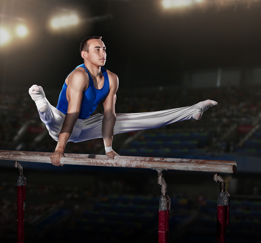 Gymnast in a blue uniform performs a straddle hold on parallel bars in a dimly lit arena.