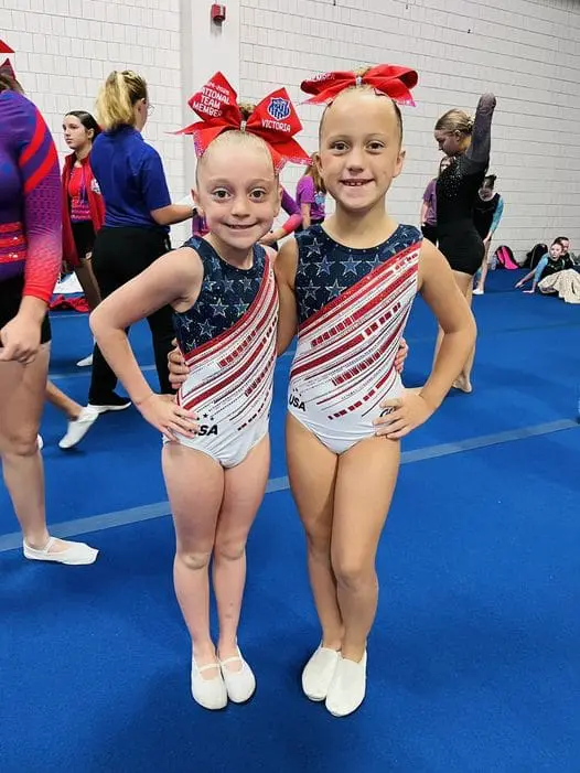 Two young girls posing for a picture in their gymnastics uniforms.