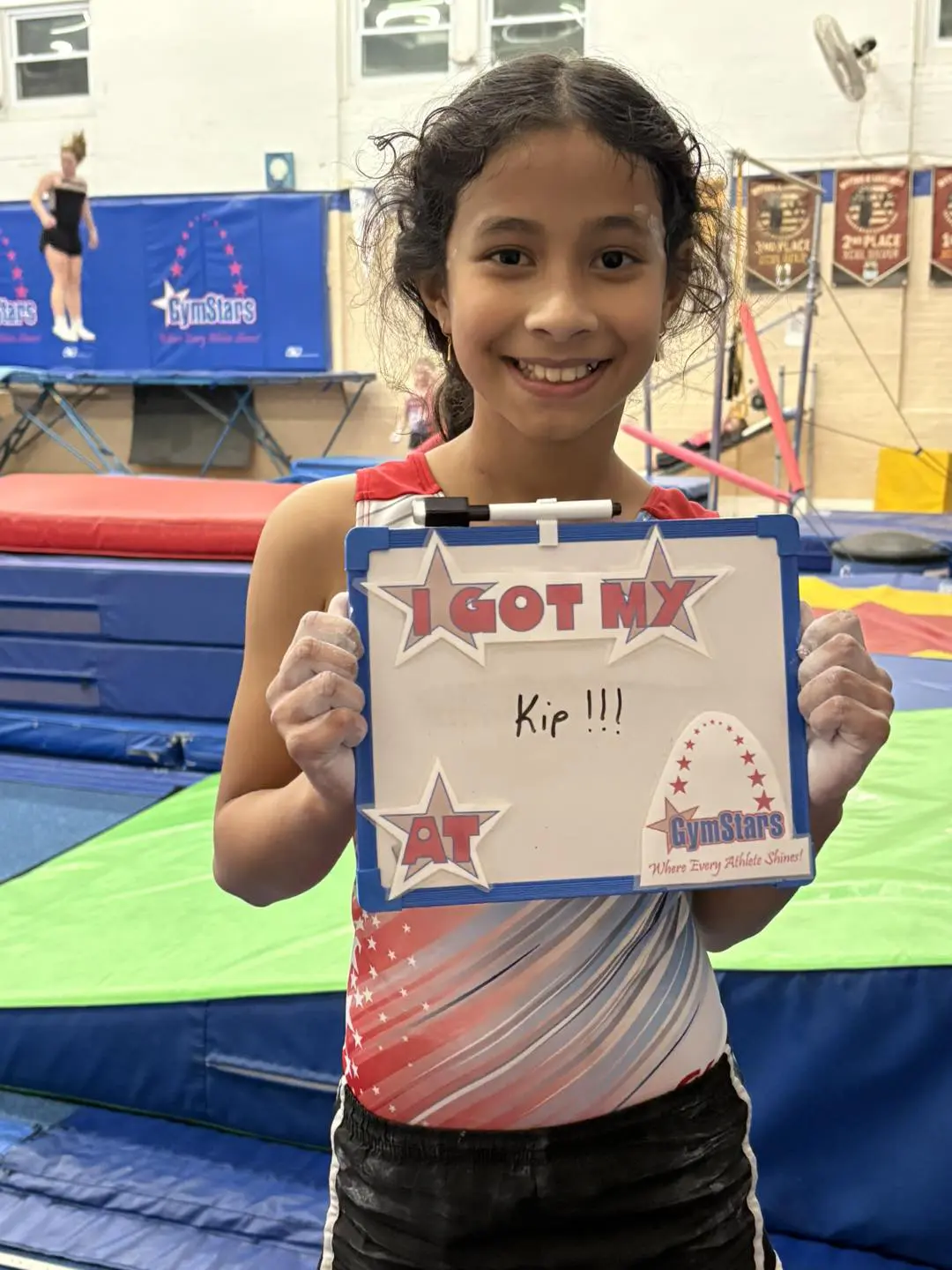 Smiling gymnast holding "I got my Kip" board