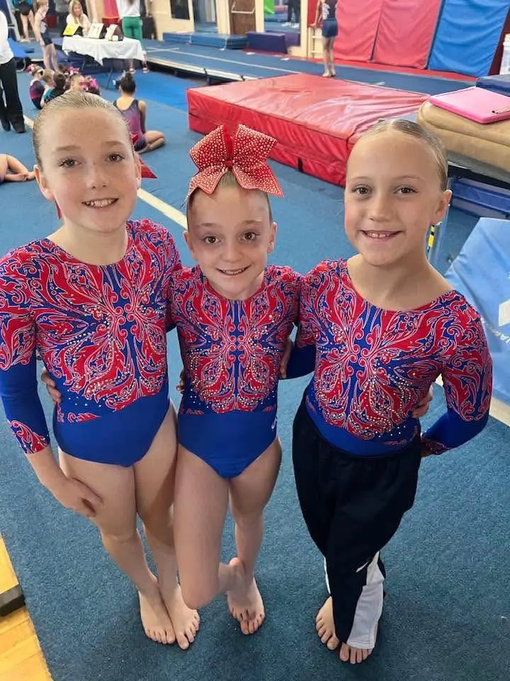 Three smiling gymnasts in red patterned leotards