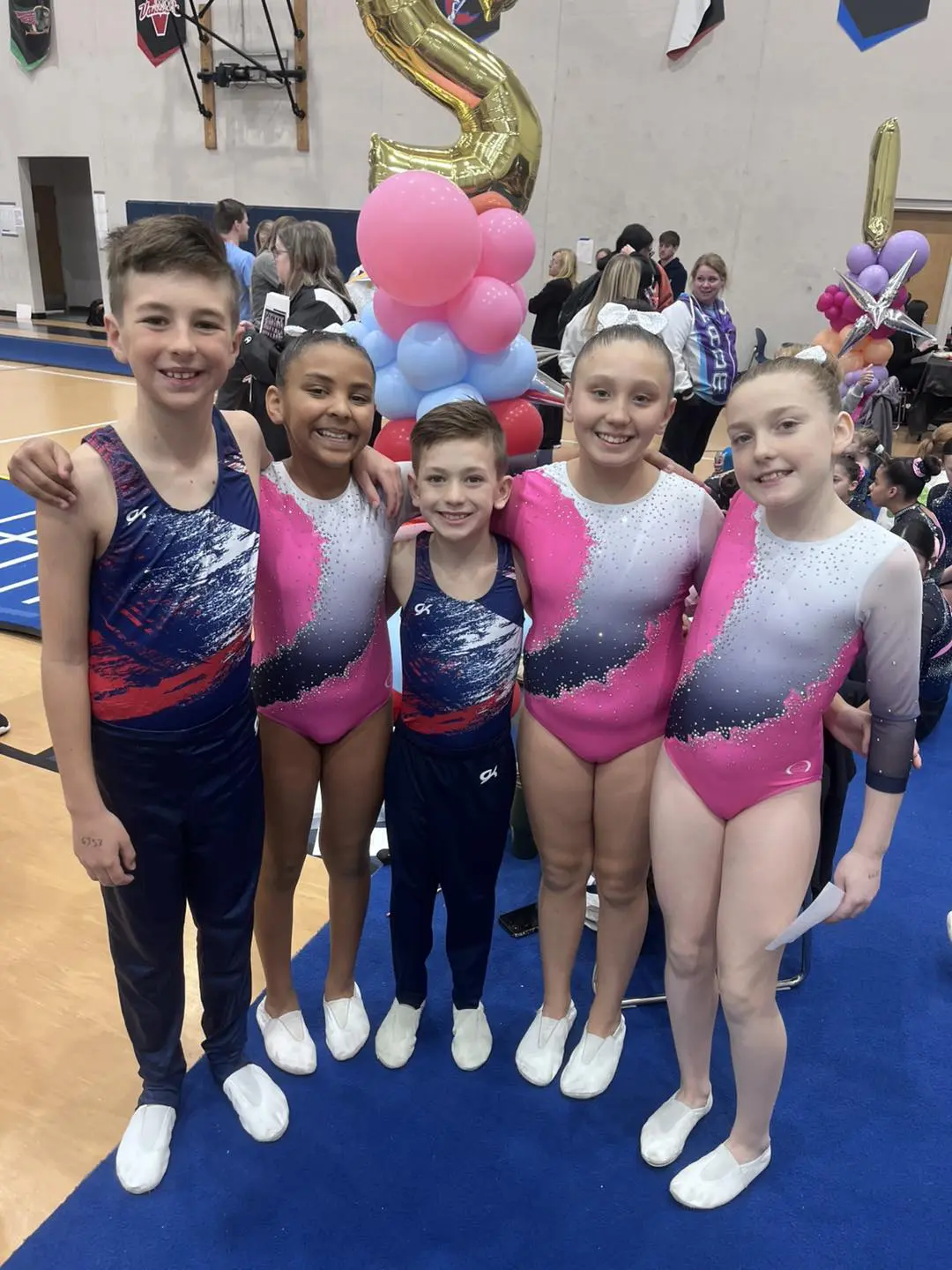 Five young gymnasts posing at competition