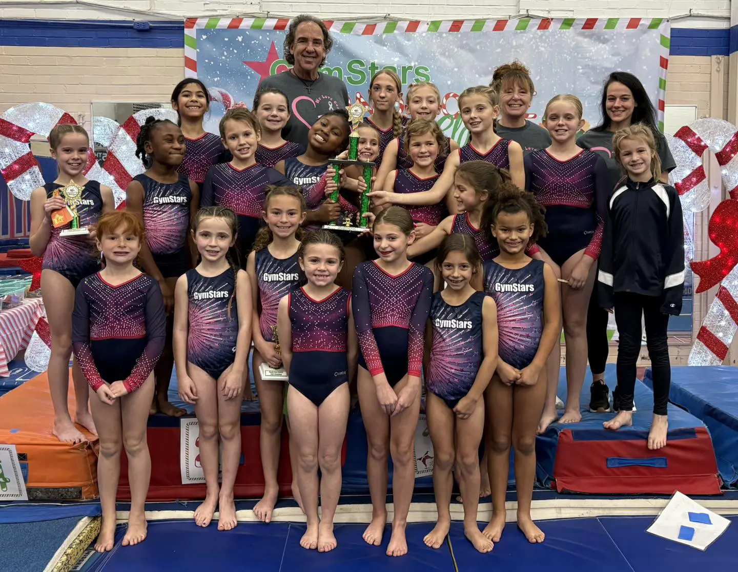 Youth gymnastics team posing with coaches, trophies