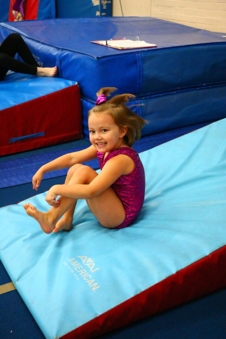 A little girl sitting on the ground in an indoor gym.