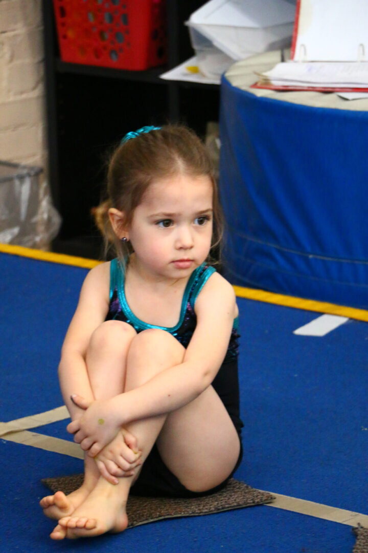 A little girl sitting on the ground in a gym.